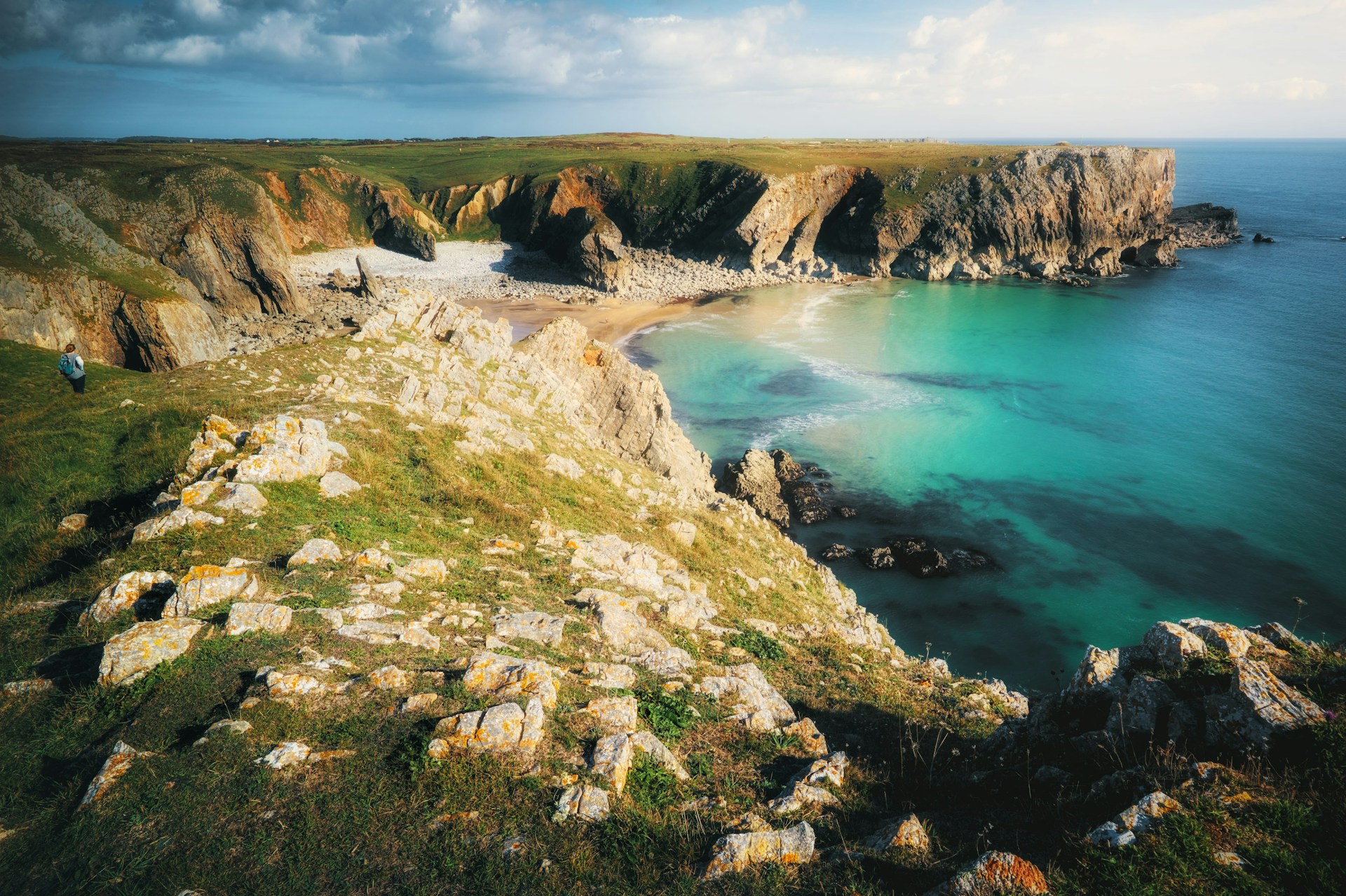 Turquoise sea below limestone cliffs on the Pembrokeshire Coast Path, with a walker on the headland